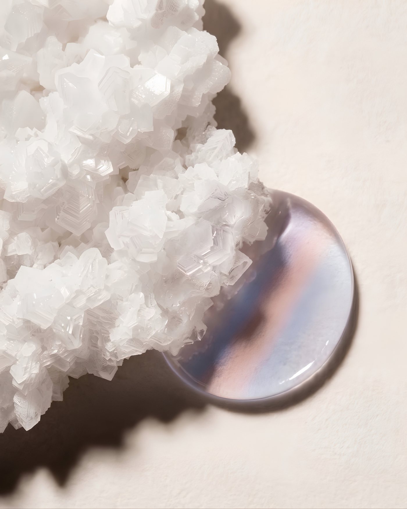Macro photograph of a translucent droplet catching soft pink and blue light against white crystal formations